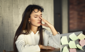 Frustrated woman sitting at her desk with her laptop open with sticky notes on back of computer.